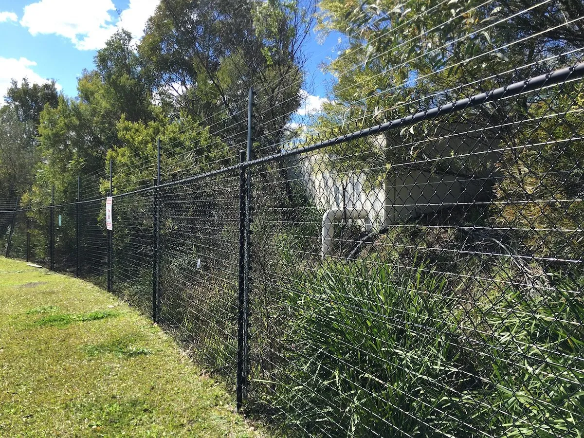 Black chainwire boundary fence running along a sloping block