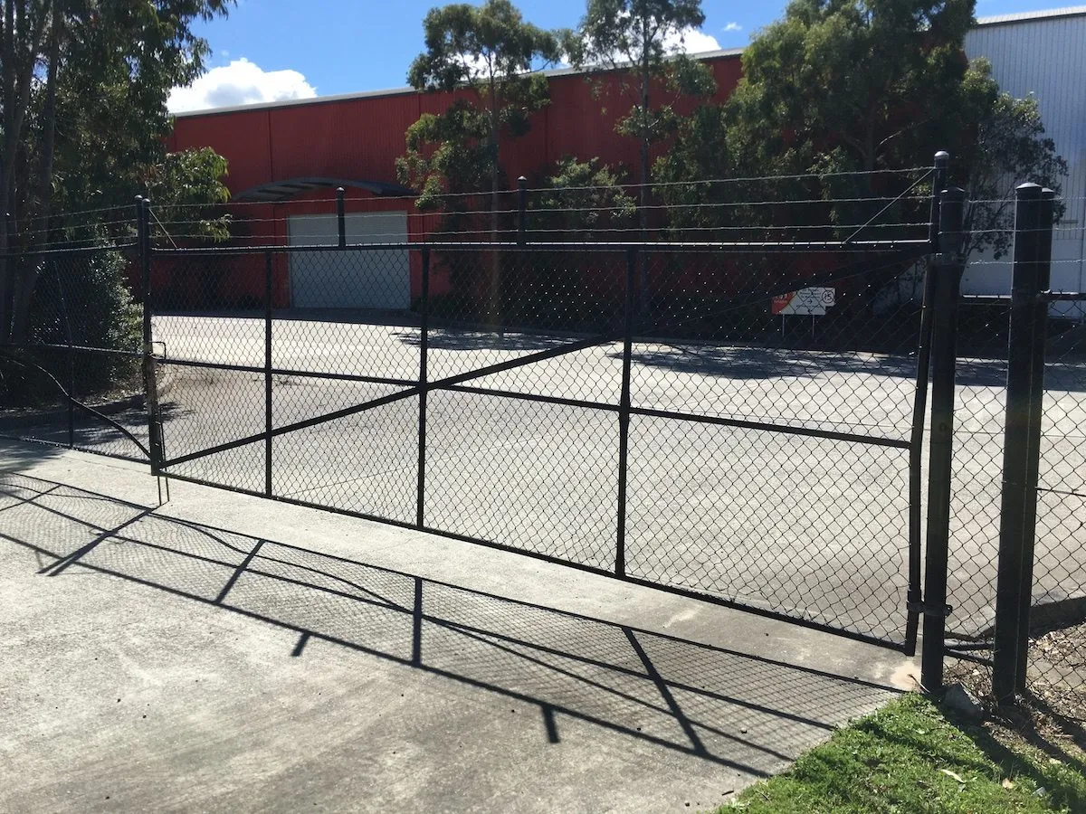Black chainwire gate with a barbed-wire top at a commercial yard
