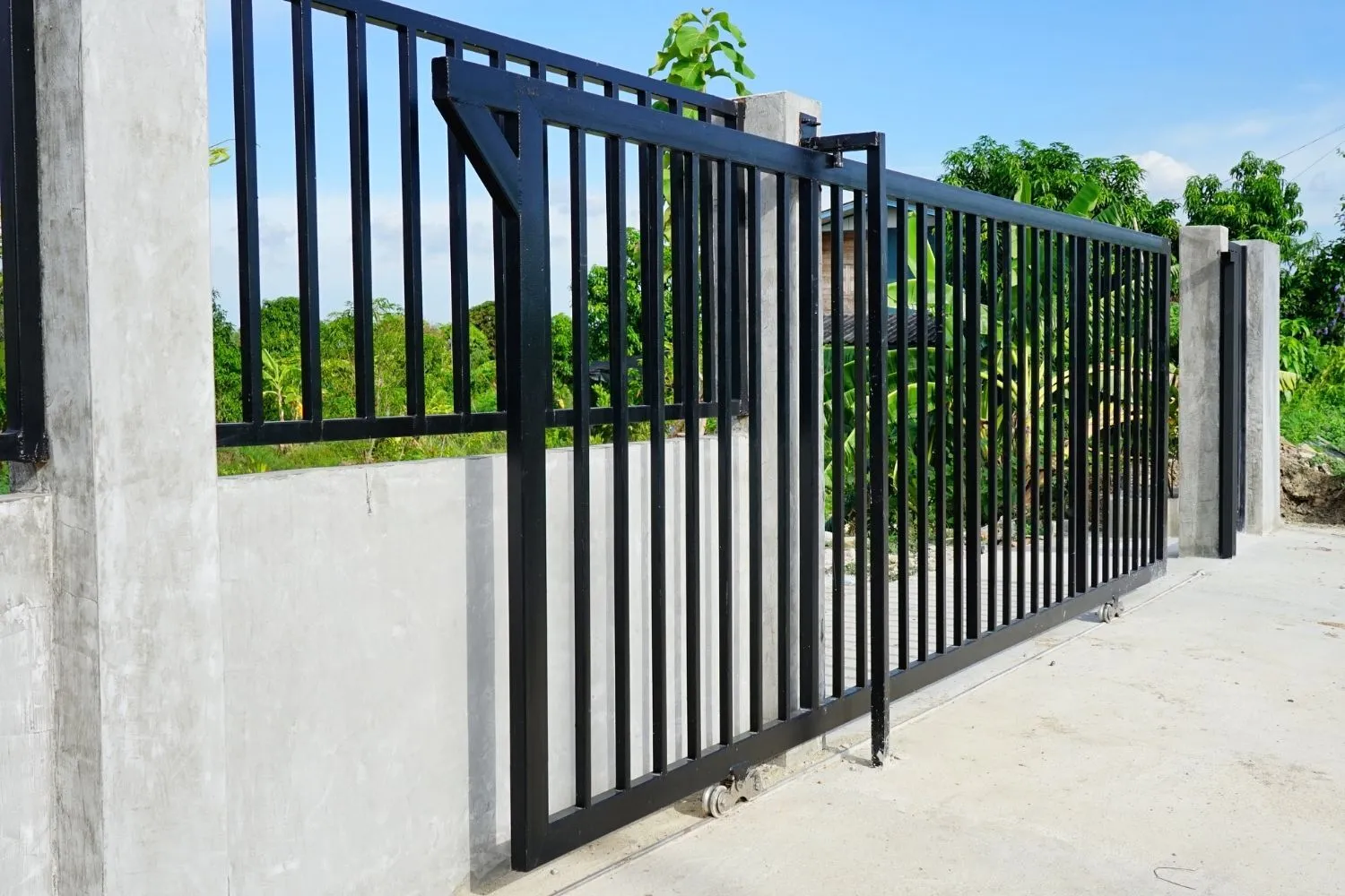 A black metal sliding gate part-open along a concrete wall.