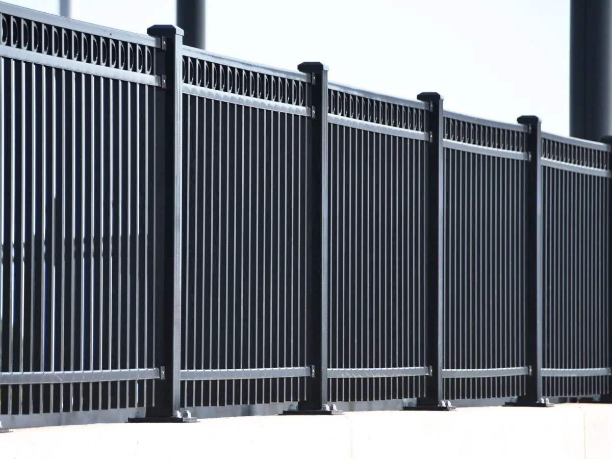 A black steel fence with vertical slats and a decorative top rail on a concrete base.