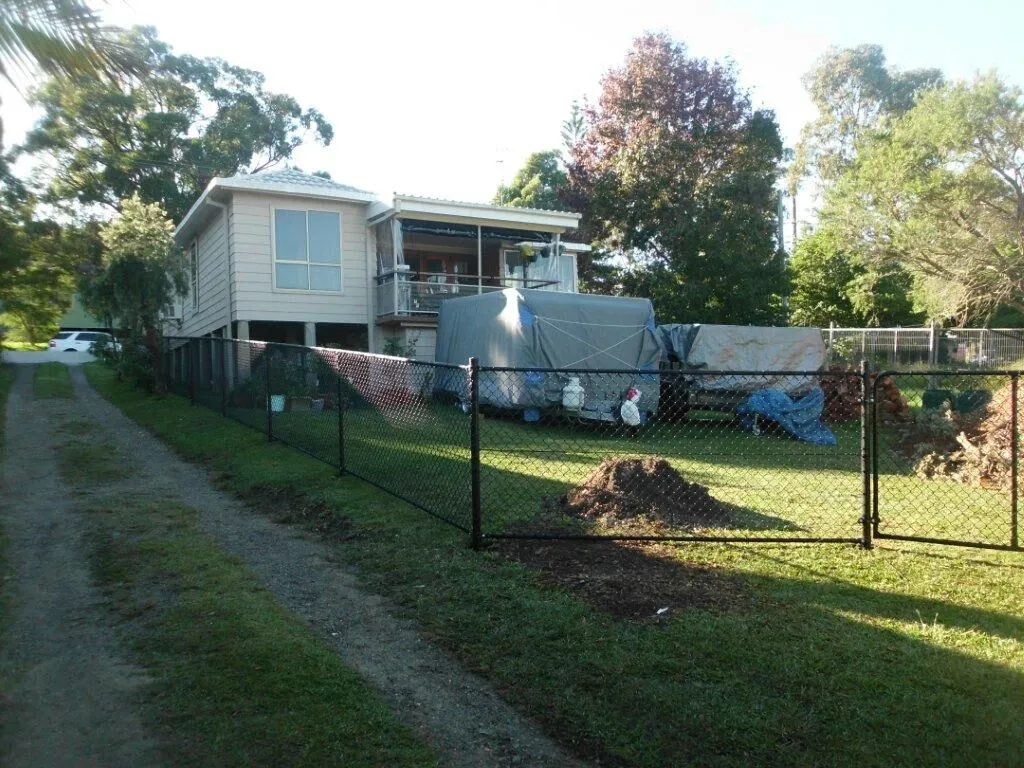 A black PVC-coated chainwire fence against green lawn and foliage.
