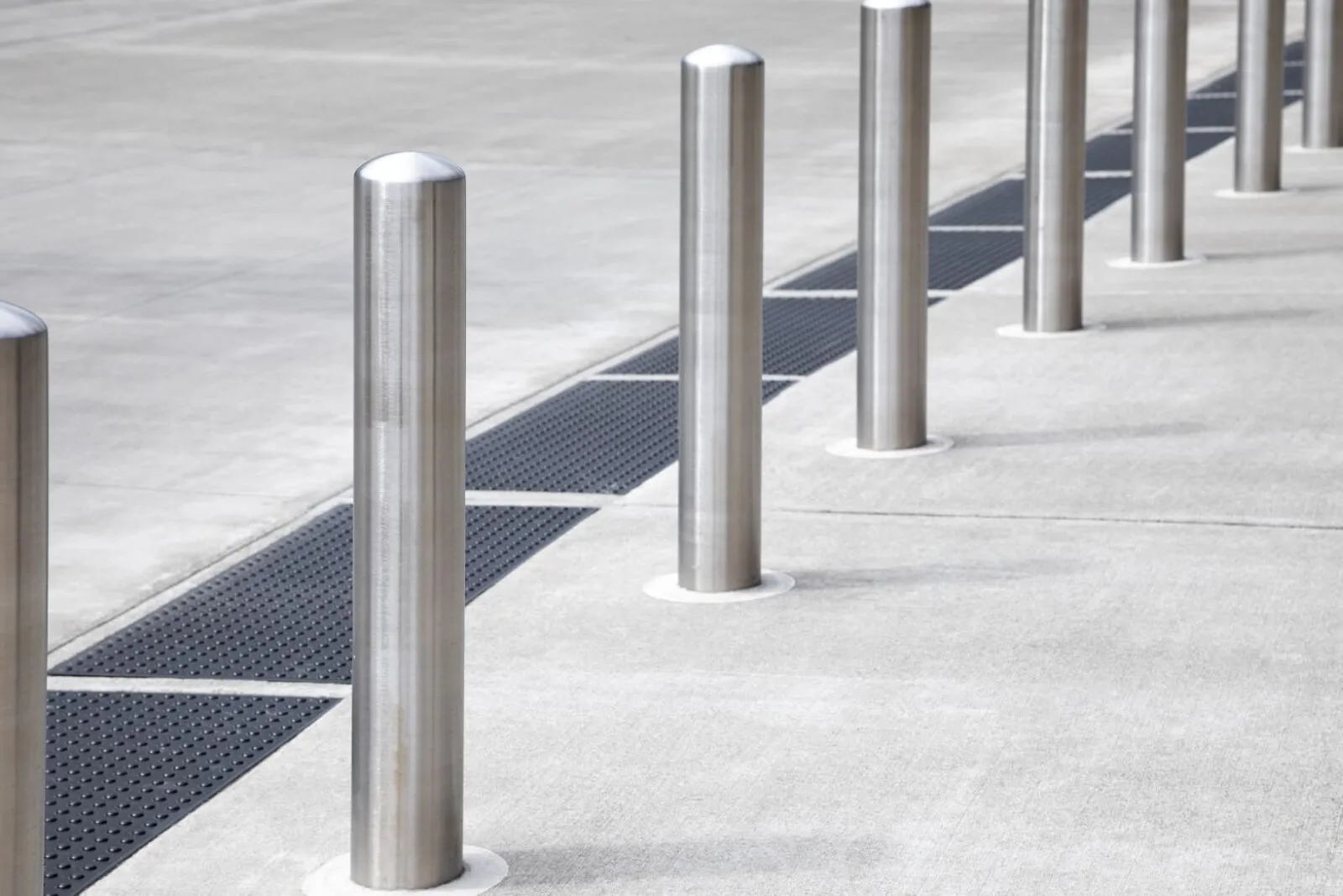 A row of silver brushed-metal bollards along a concrete walkway