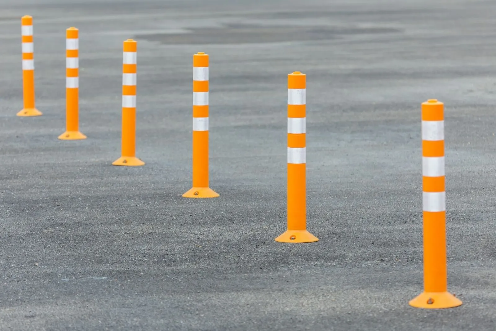 A row of orange flexible delineator posts with white reflective bands on asphalt