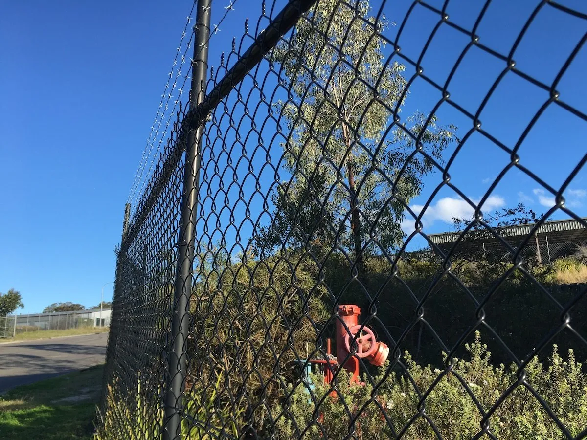 Black chainwire security fence with a barbed-wire top at an industrial site