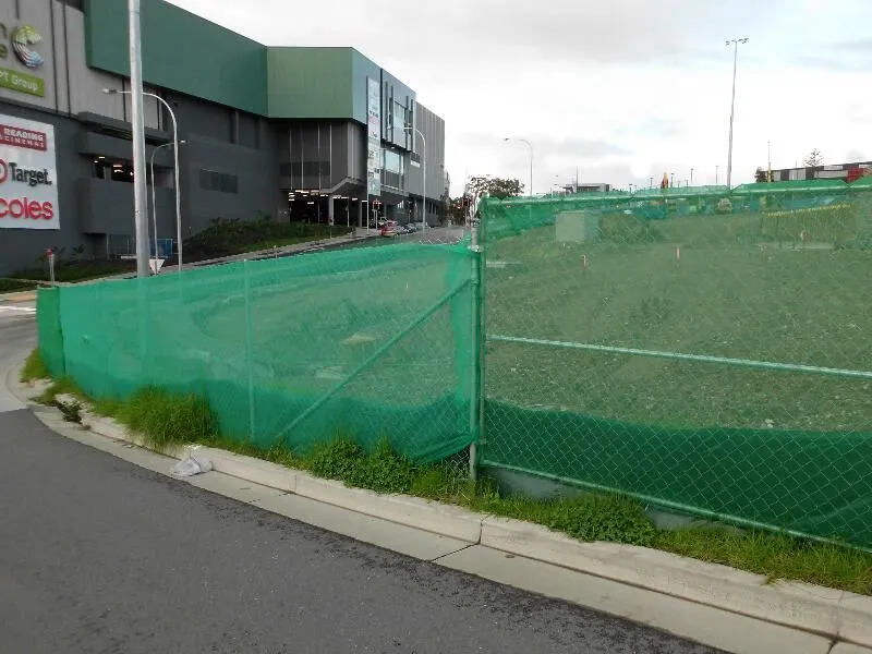 Temporary construction fencing with green shade cloth along a worksite.