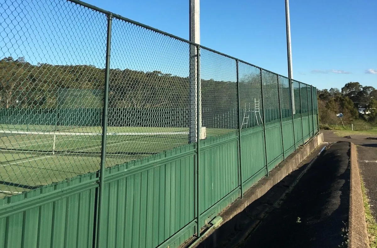 Green chainwire court fencing with a solid metal base along a sports court