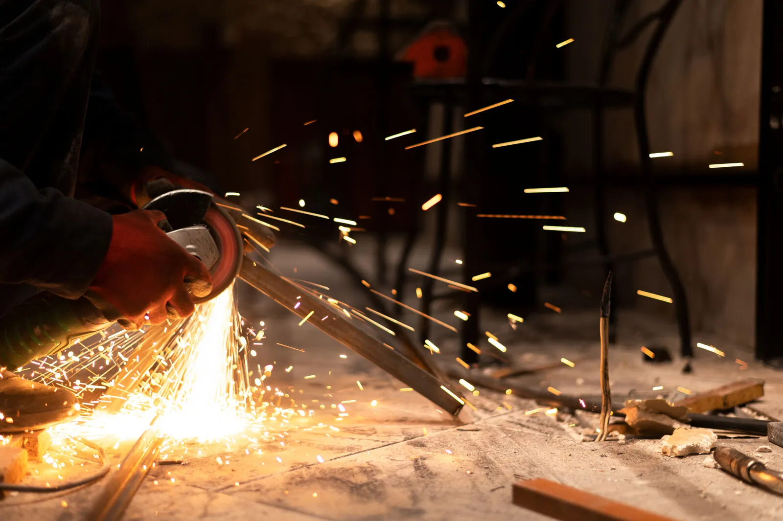 A worker cutting a steel bar with a power grinder, sparks flying across the workshop floor