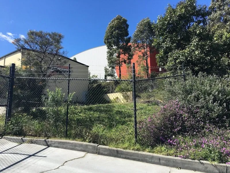 Black chainwire boundary fence running along a sloping industrial block