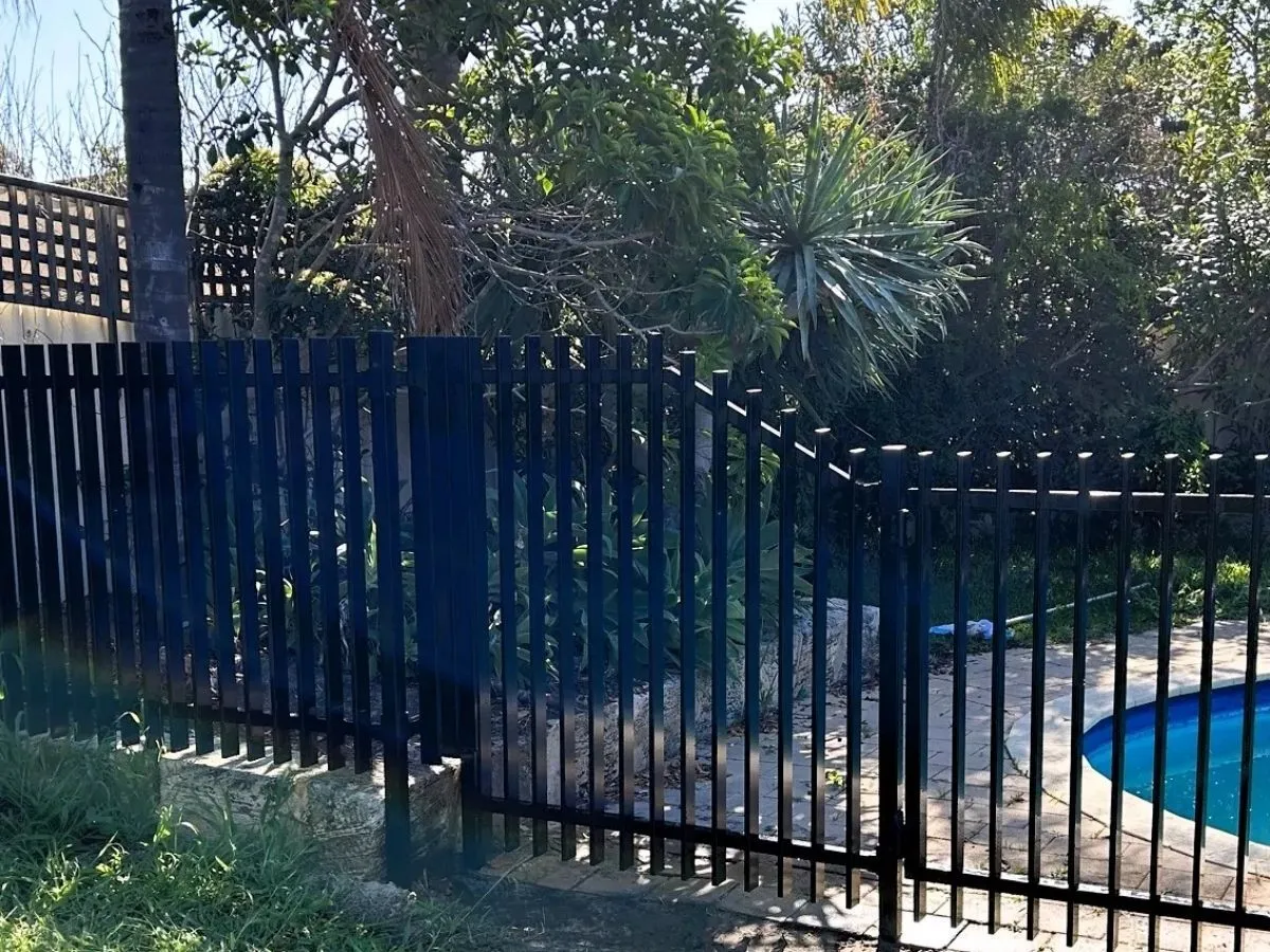 A steel fence raked to follow the fall of sloping ground.