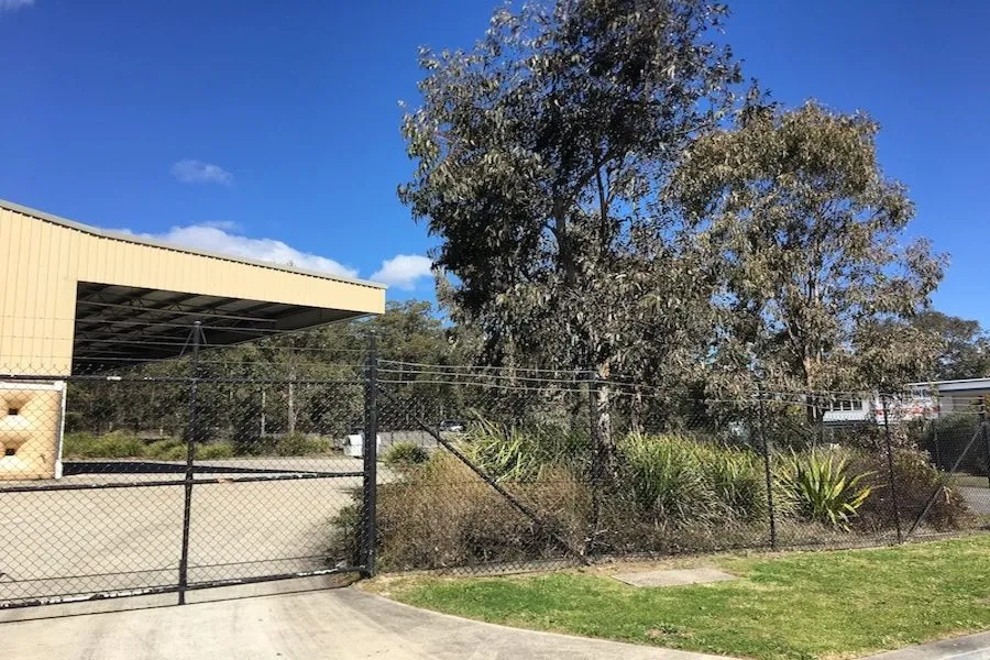 Black chainwire gates with a barbed-wire top at a rural industrial yard