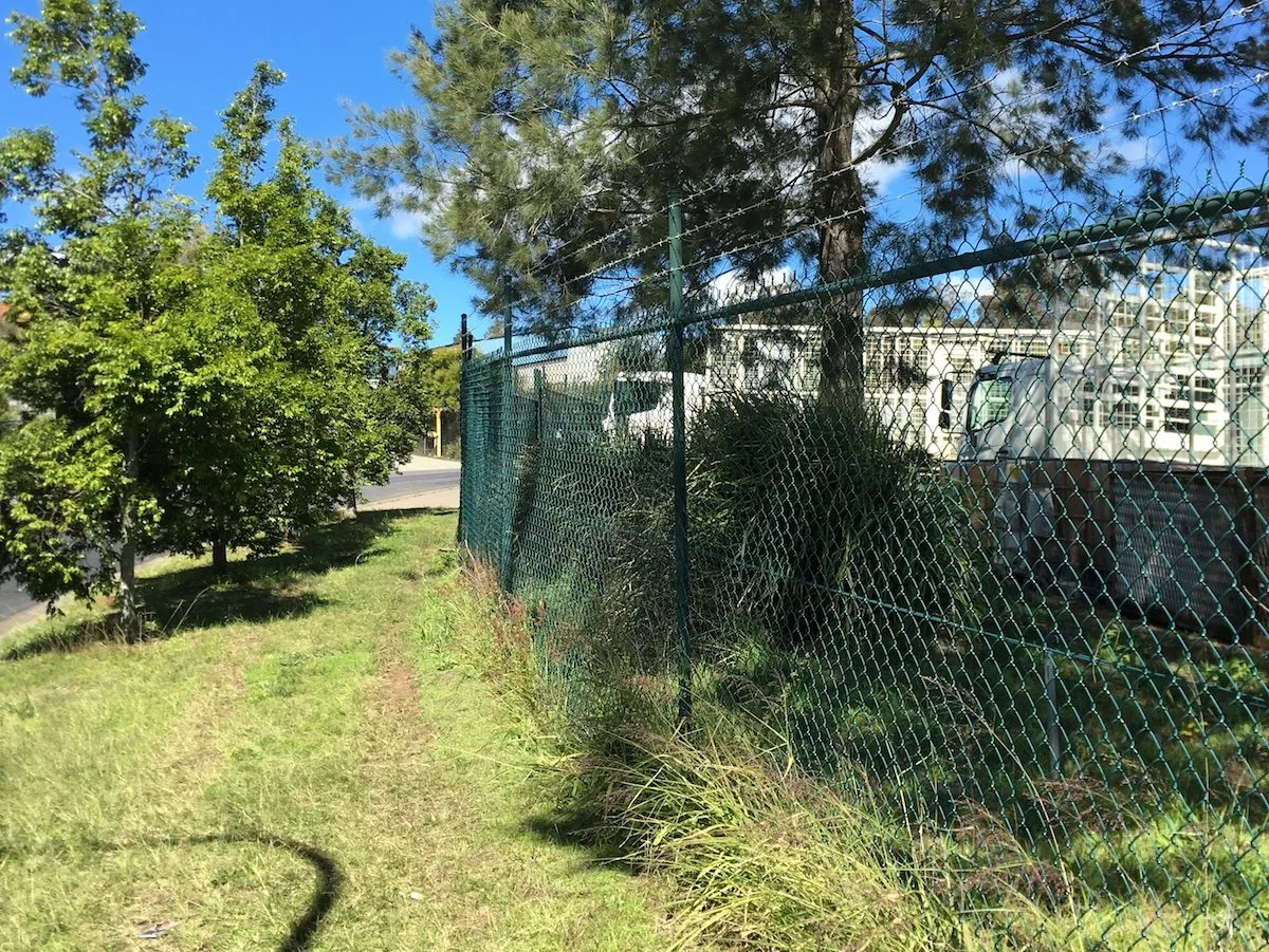 Green PVC-coated chainwire fence along an industrial yard boundary