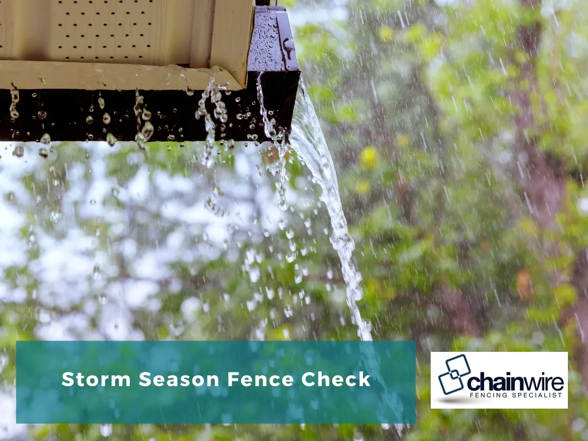 Heavy rain pouring off a roof gutter in front of blurred green trees, titled Storm Season Fence Check