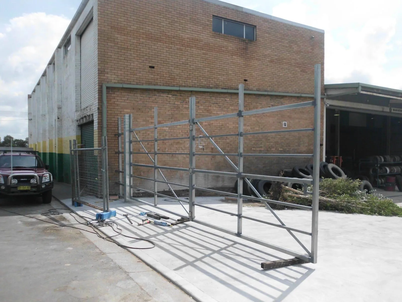 A swinging bi-fold gate at a fenced vehicle entry.