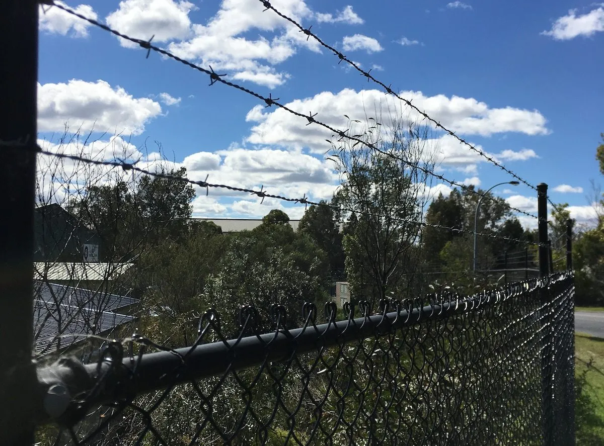 Black chainwire fence topped with barbed wire