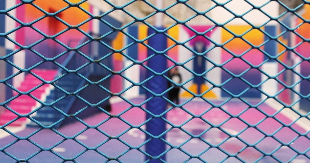 A blue diamond-patterned mesh fence in the foreground with a vibrant pink, purple, and orange basketball court