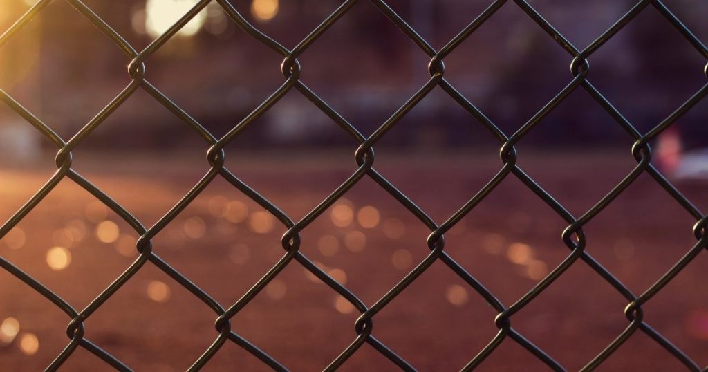 A close-up of a chain-link fence against a blurred, sunlit orange background.