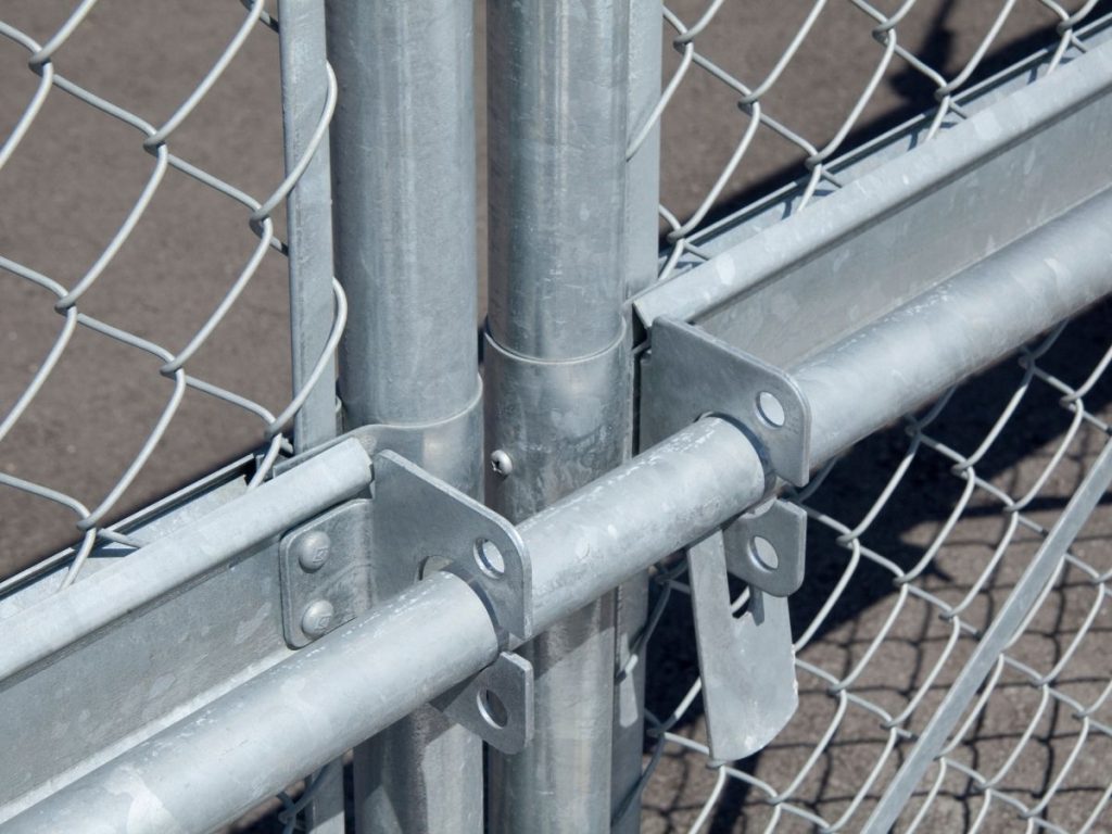 Close-up of a galvanised chain-link fence gate featuring a metal sliding latch and horizontal support rails.