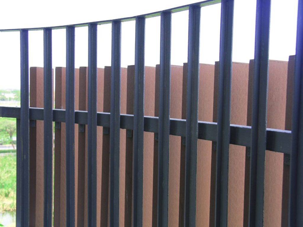 A close-up shot of a dark metal fence with vertical bars, partially backed by reddish-brown wooden slats.