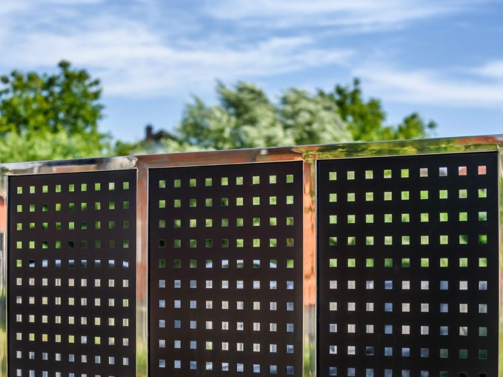 Modern metal fence with square-perforated dark panels and a reflective chrome frame