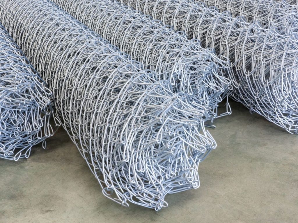 Several rolls of galvanised chain-link fencing mesh stacked on a concrete floor.