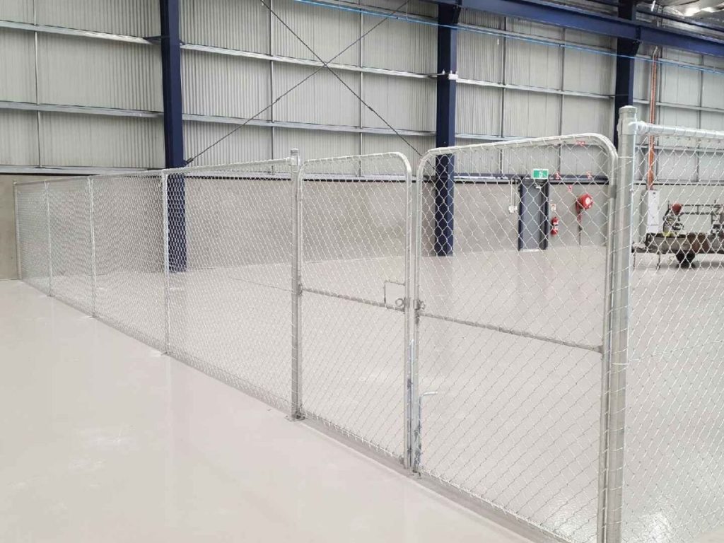 A galvanised chain-link fence with a double gate installed inside a warehouse with a polished concrete floor.