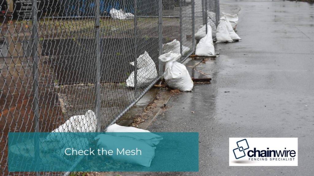 What to Check After Storm Damage to Your Fence - Storm damage White sandbags lining the base of a chain-link fence on a wet, paved walkway to prevent storm damage