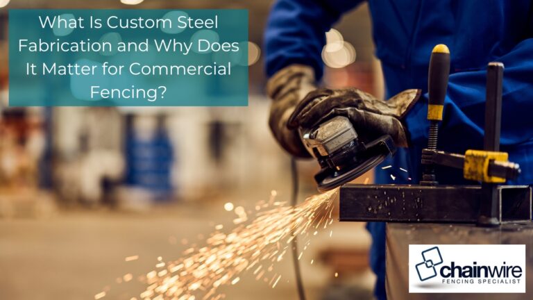 A worker in blue coveralls uses an angle grinder on a clamped steel beam, producing a shower of sparks in a fabrication workshop.